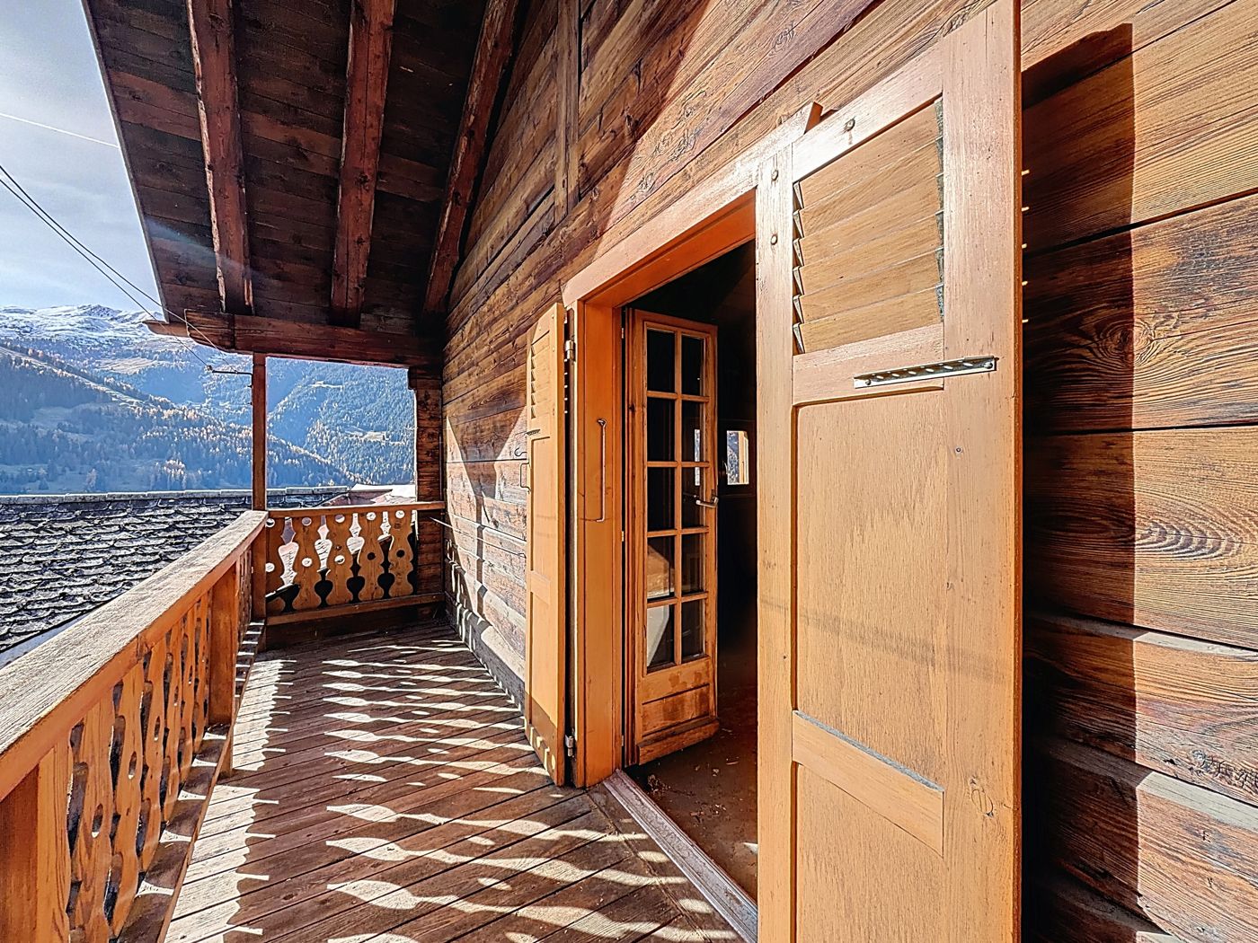 Le balcon en bois ouvragé, porte vitrée et volet, montagnes en arrière-plan.