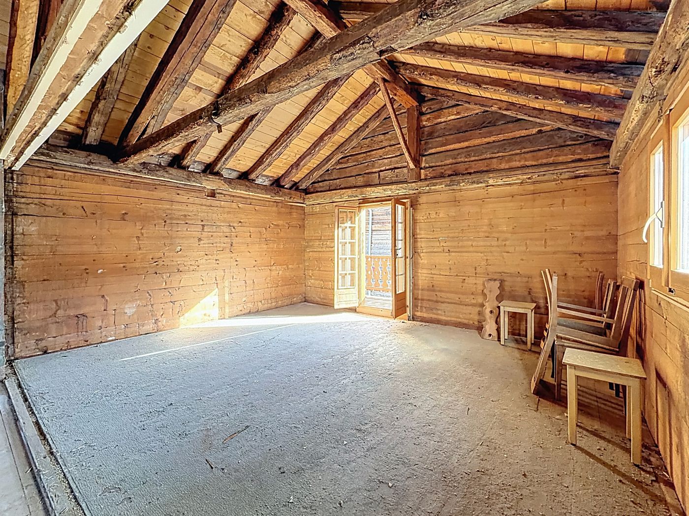 Les combles baignés de soleil, charpente en bois, porte-fenêtre ouverte vers le balcon.
