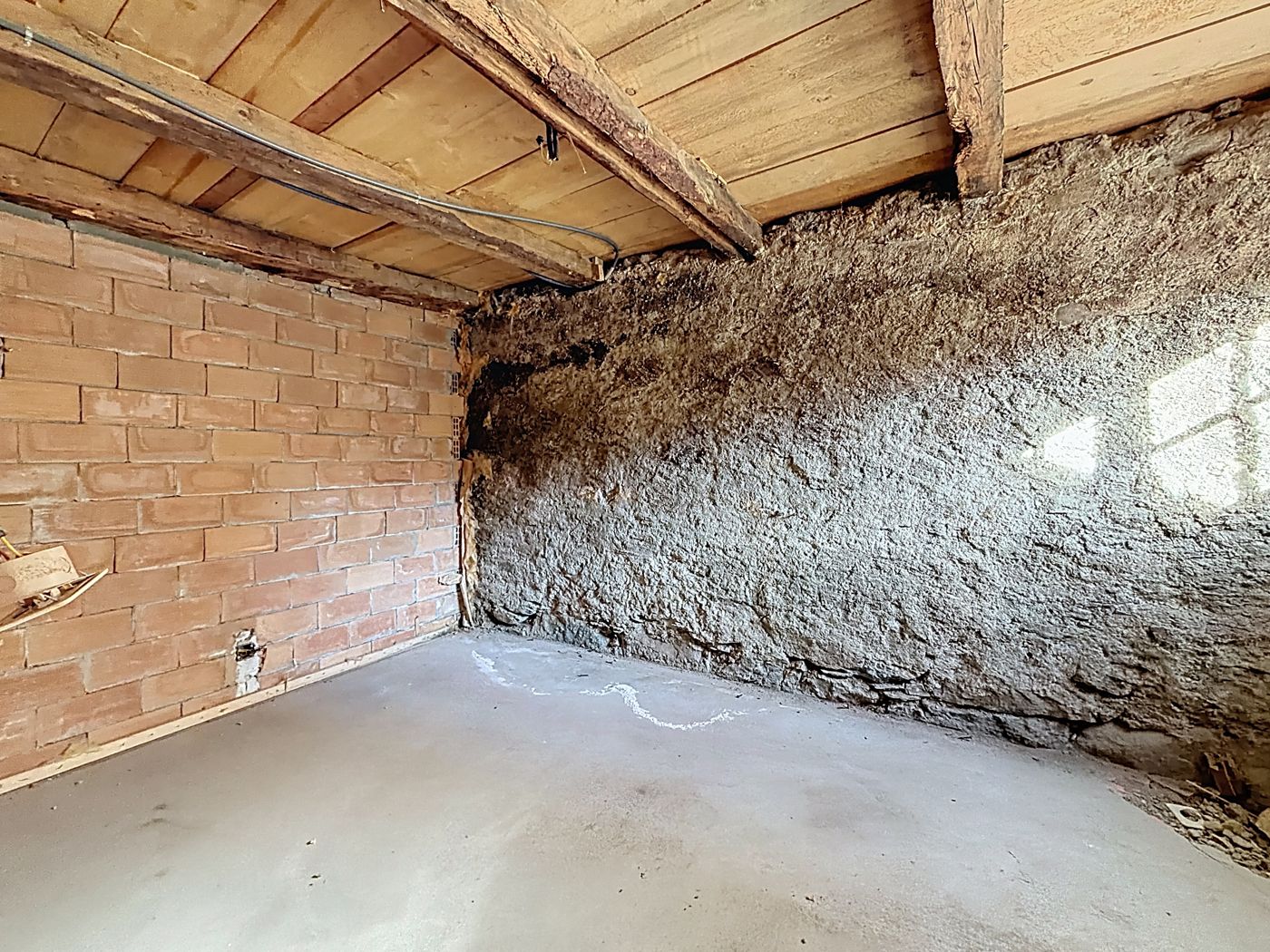 Rez-de-chaussée : mur de pierre, poutres et plafond en bois, cloison en brique à gauche.