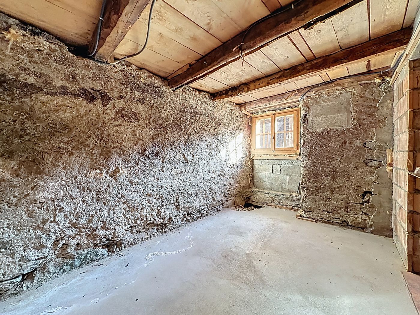 Autre vue du rez-de-chaussée : mur de pierre, fenêtre, poutres apparentes.