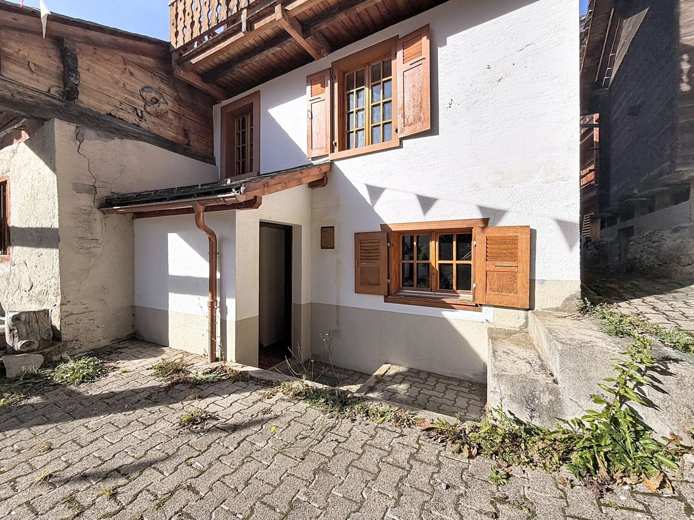La cour pavée devant l'entrée : porte d'entrée, fenêtres à volets de bois et avant-toit.