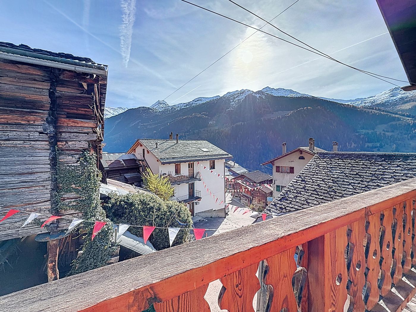Vue depuis le balcon ouvragé : toits d'ardoise du village, maisons de Sarreyer et sommets enneigés sous le soleil.